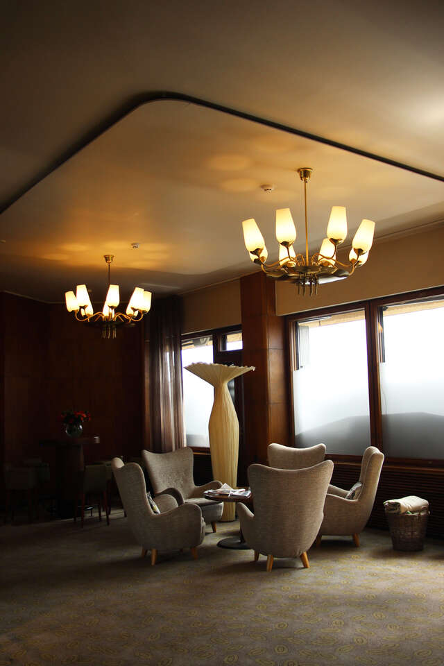 Tall coffee table surrounded by beige armchairs.