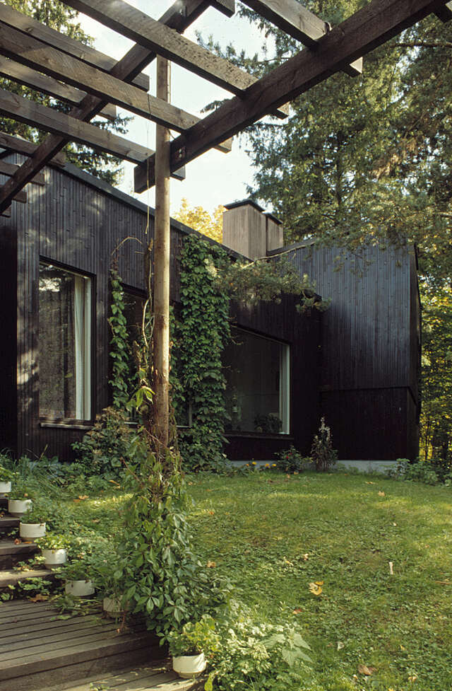 Pergola and low steps in front of dark stained wooden house