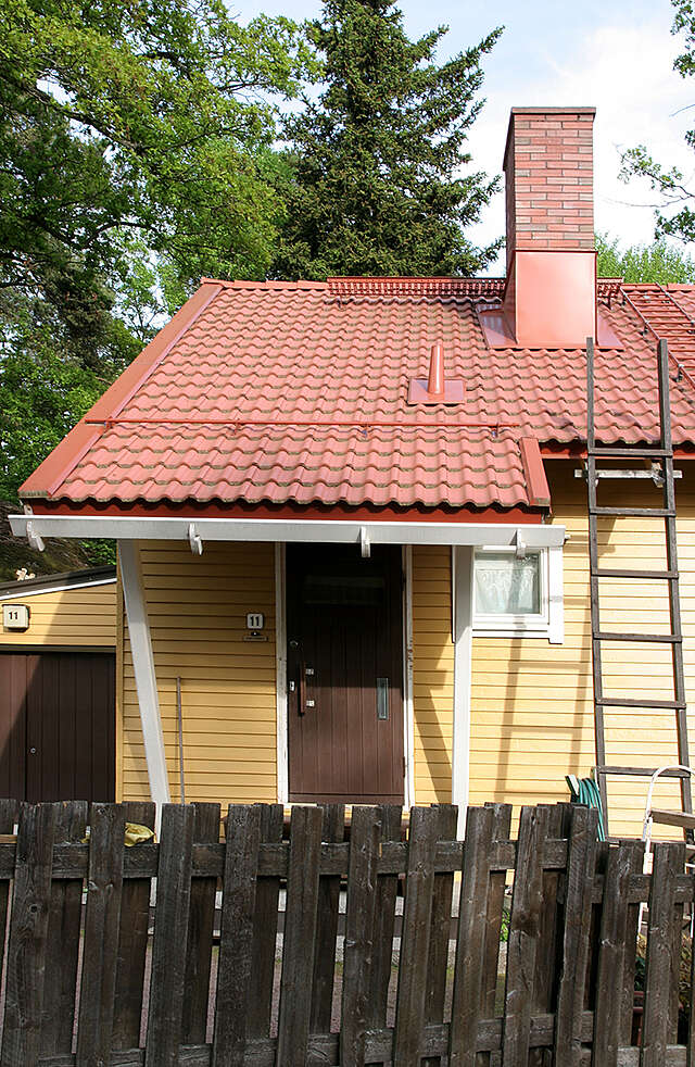 Yellow wooden house with a red roof extending over the front door.